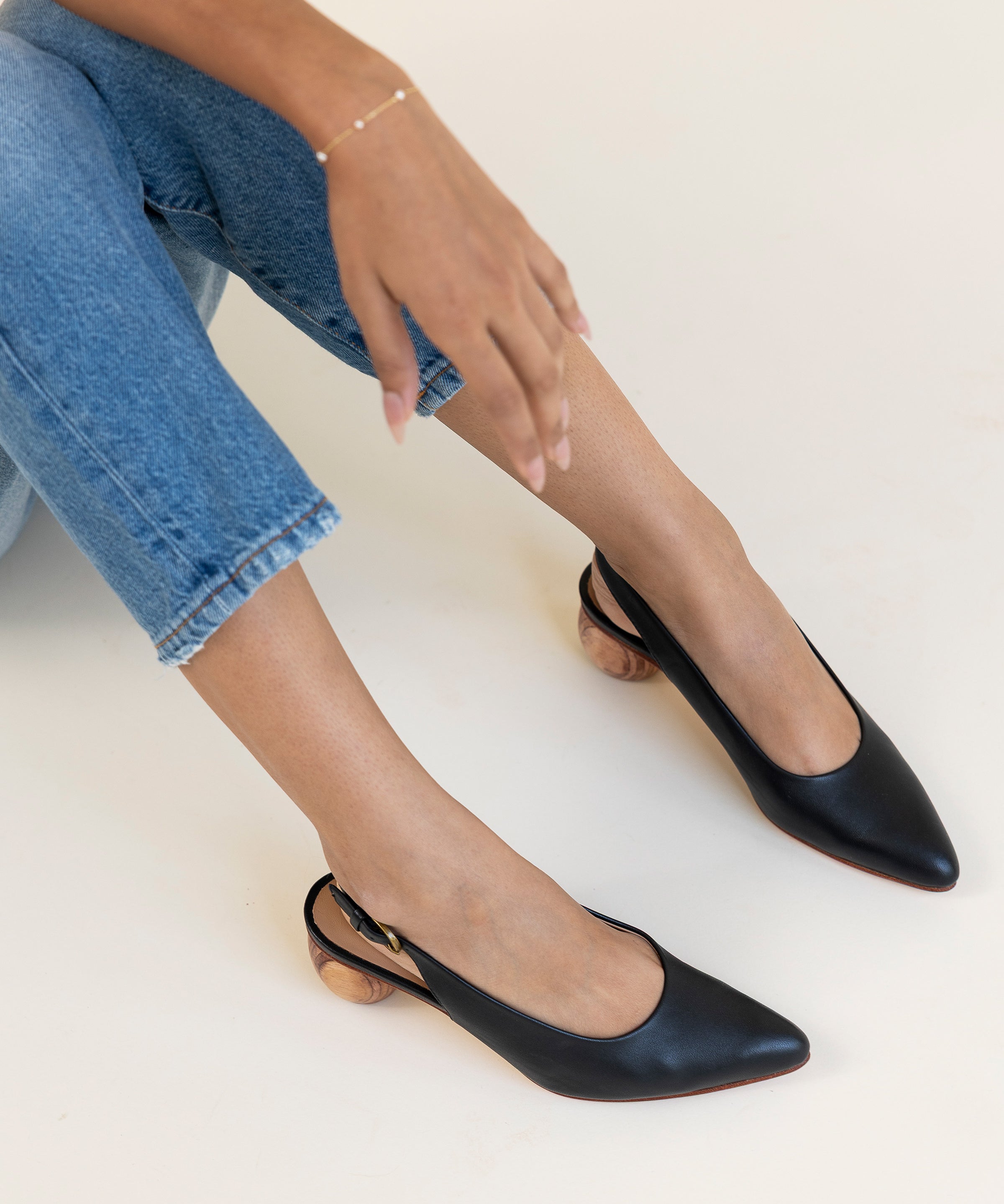 Black slingback shoes worn with blue jeans on a white background