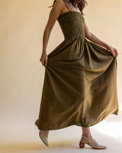 Woman wearing a long olive green dress with cream colored slingback pumps against a beige background