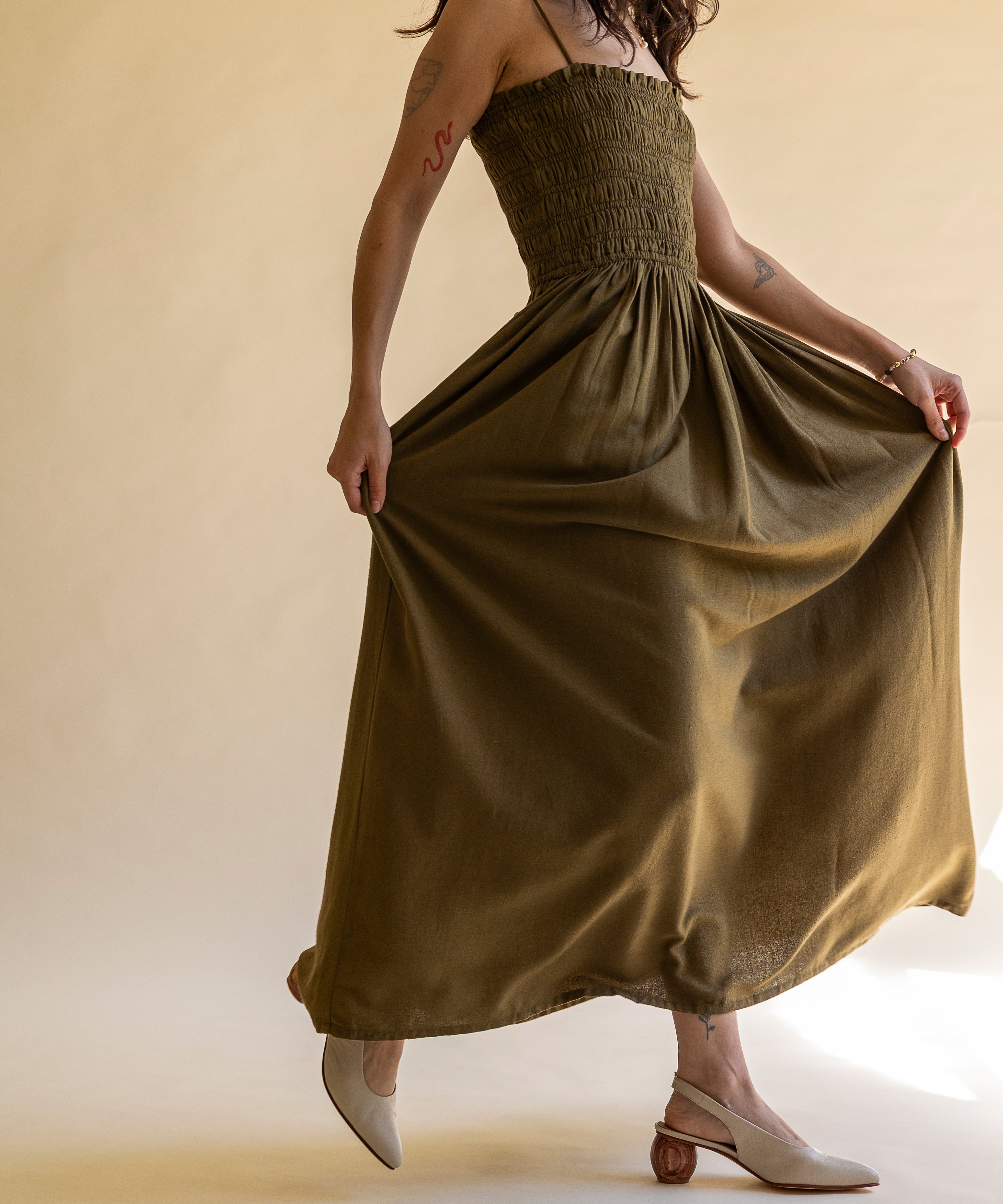 Woman wearing a long olive green dress with cream colored slingback pumps against a beige background