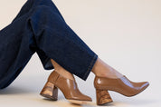 Brown leather shoes worn with dark jeans on a light background
