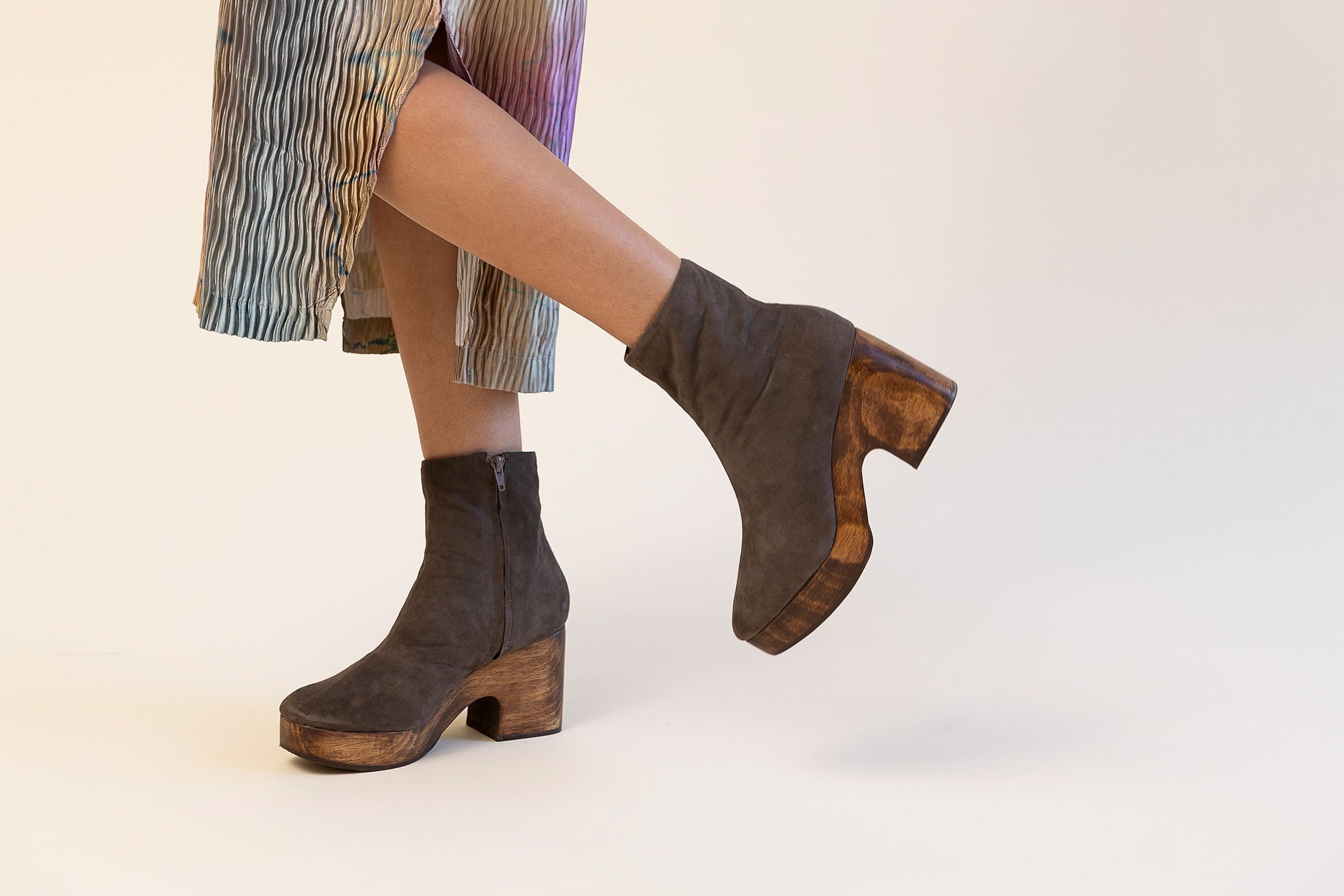 Grey suede clog boots with a wood platform worn with a striped dress on a white background