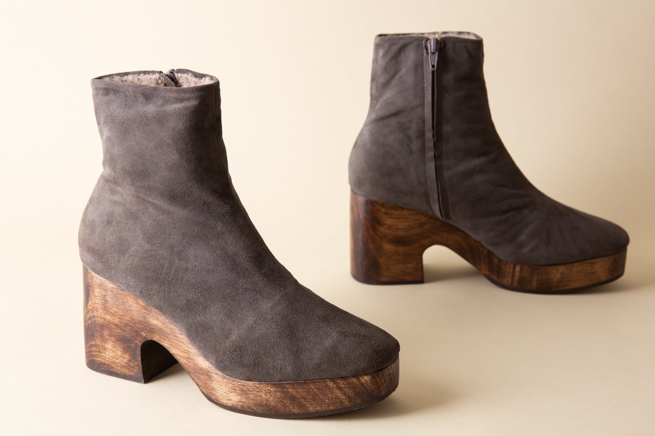 Pair of gray suede ankle boots with wooden soles on a beige background