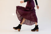 Model wearing a burgundy skirt and black suede clog boots on a white background