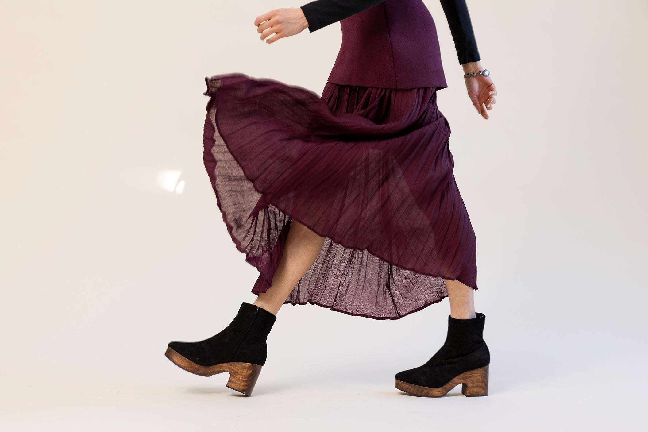 Model wearing a burgundy skirt and black suede clog boots on a white background