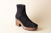 Black suede ankle boot with wooden heel and platform on a beige background