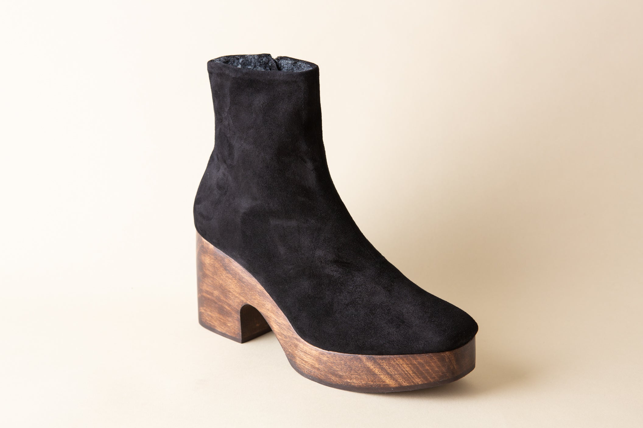 Black suede ankle boot with wooden heel and platform on a beige background