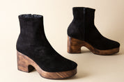 Black suede ankle boots with wooden platforms on a beige background