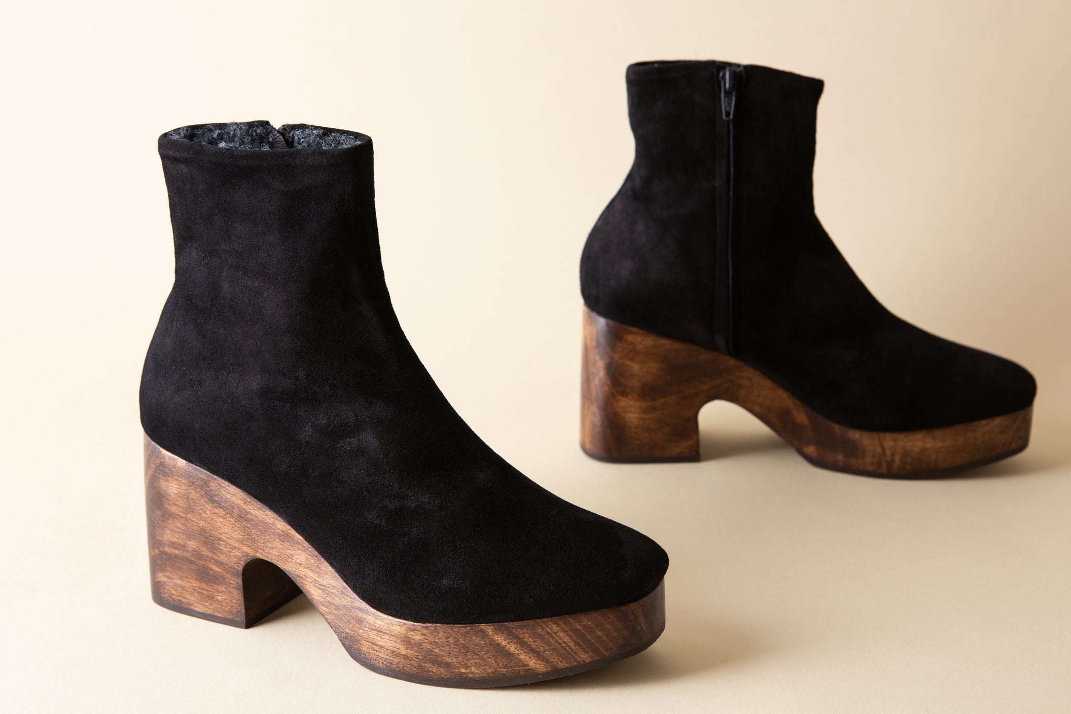 Black suede ankle boots with wooden platforms on a beige background