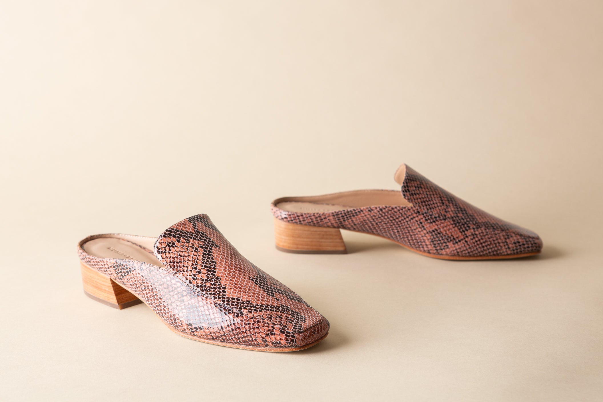 Pair of snake print mules on a beige background