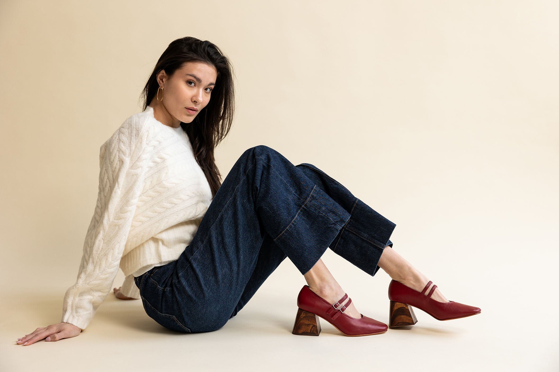 Model wearing an ivory sweater, dark jeans, and red mary jane pumps with a wooden heel.