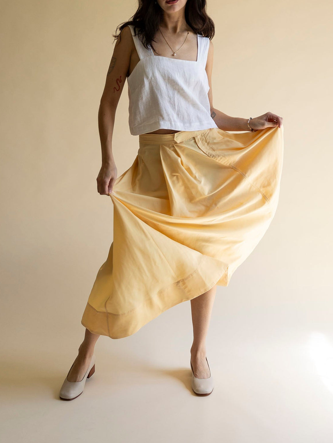 Woman wearing a white top and yellow skirt against a beige background