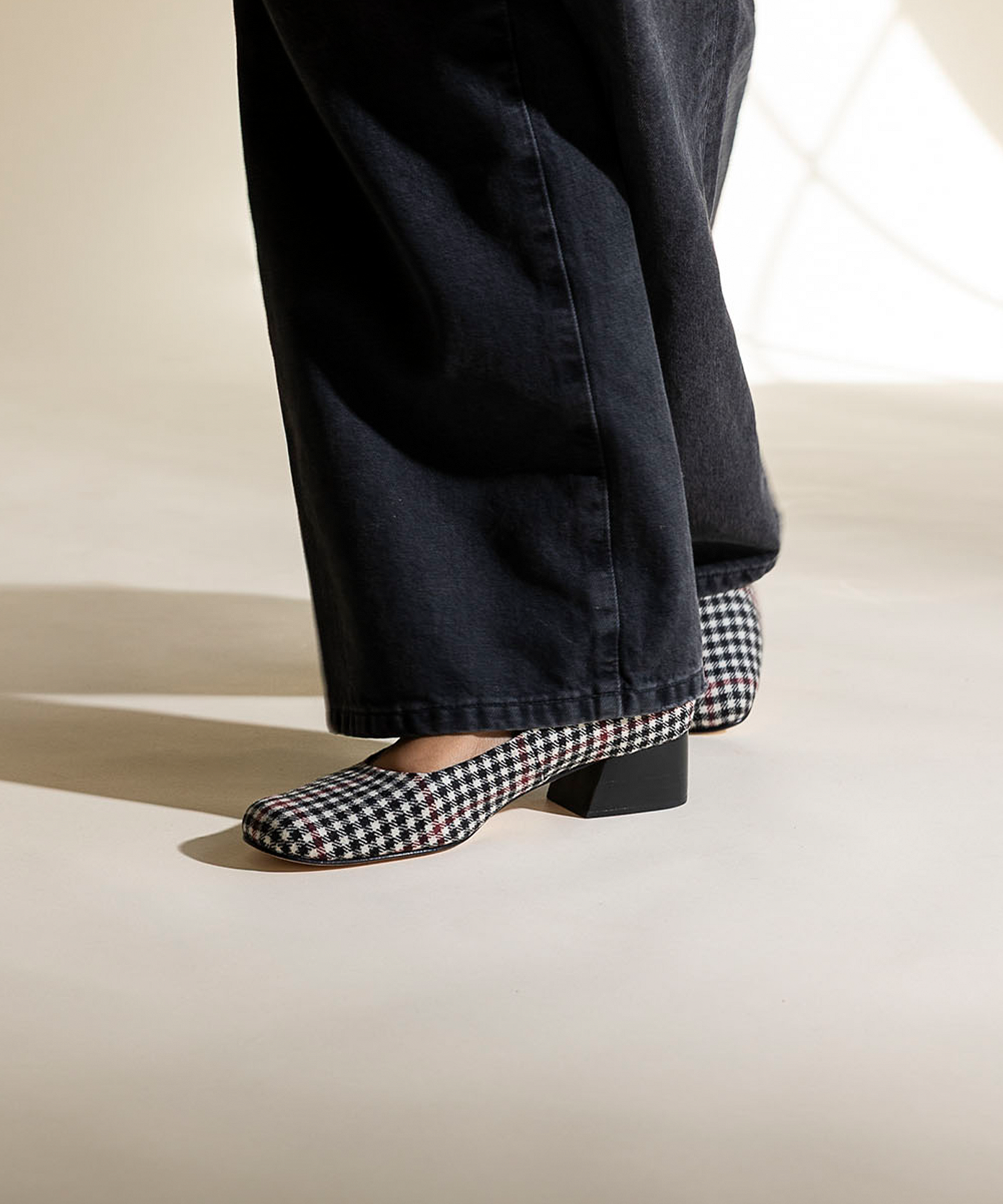 Person wearing black pants and plaid shoes on a light background