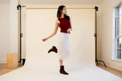 Woman posing in a studio with white backdrop and wooden floor.
