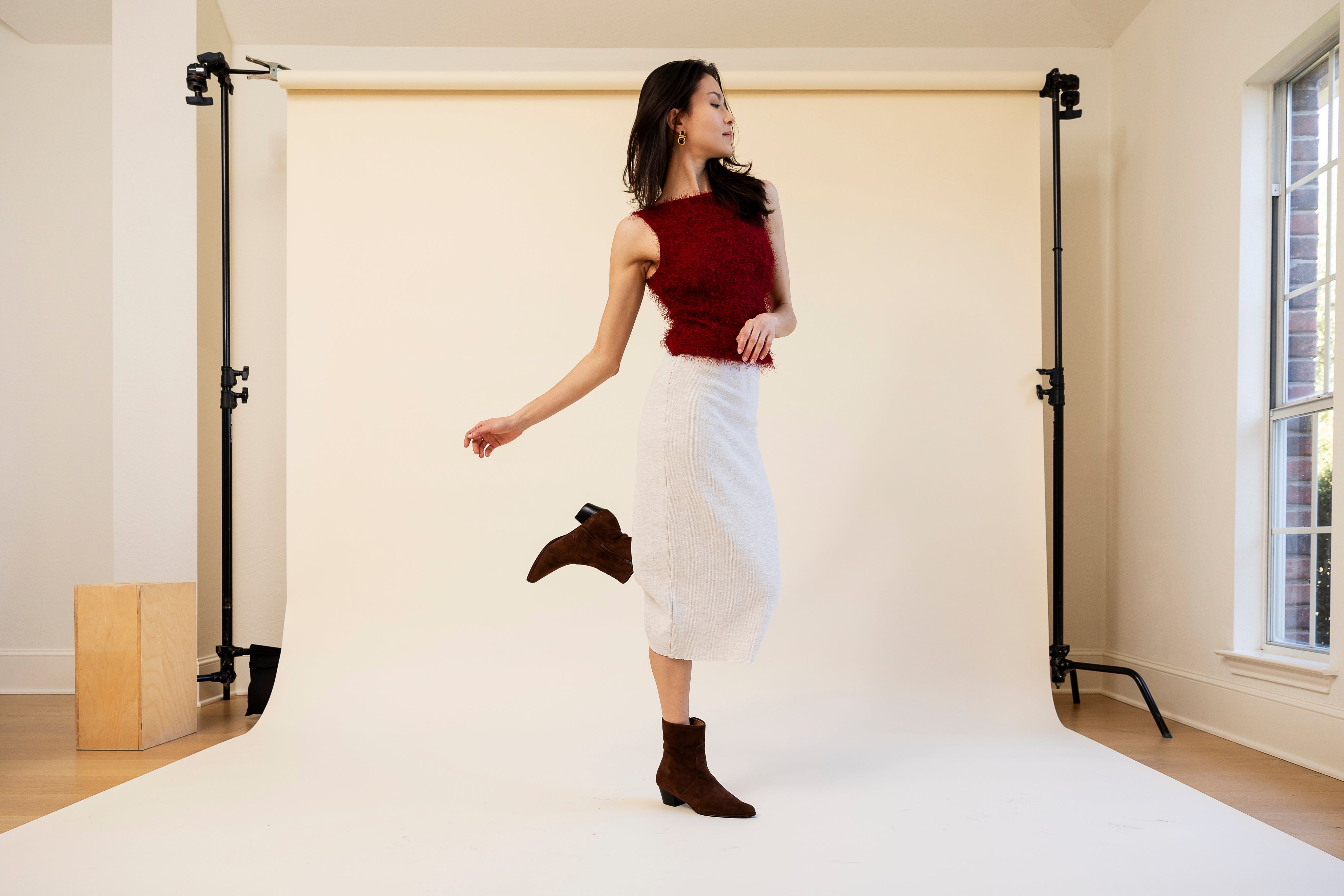 Woman posing in a studio with white backdrop and wooden floor.