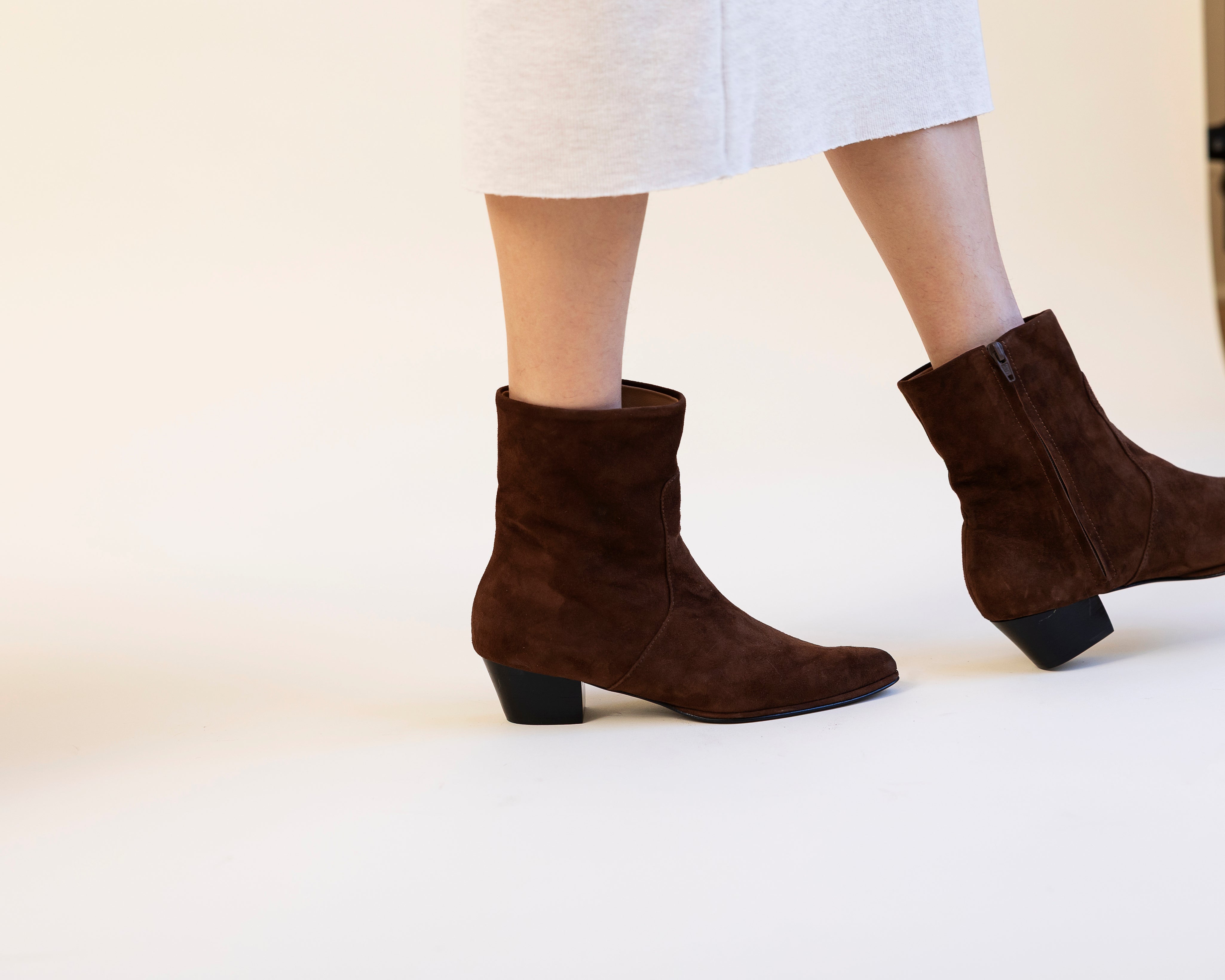 Brown ankle boots worn with a white skirt on a light background