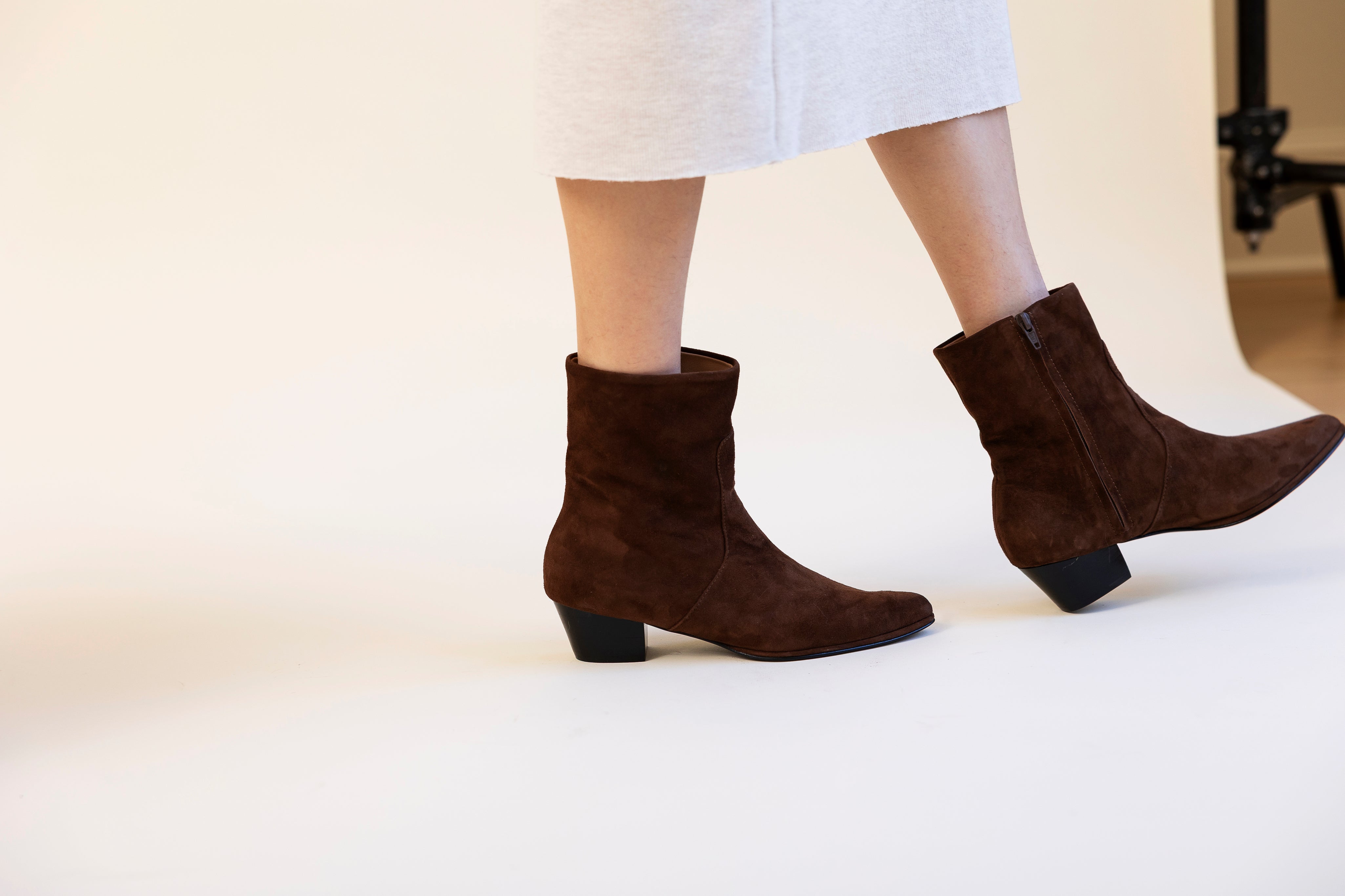 Brown ankle boots worn with a white skirt on a light background