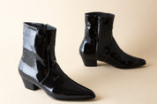 Pair of black patent leather ankle boots on a beige background