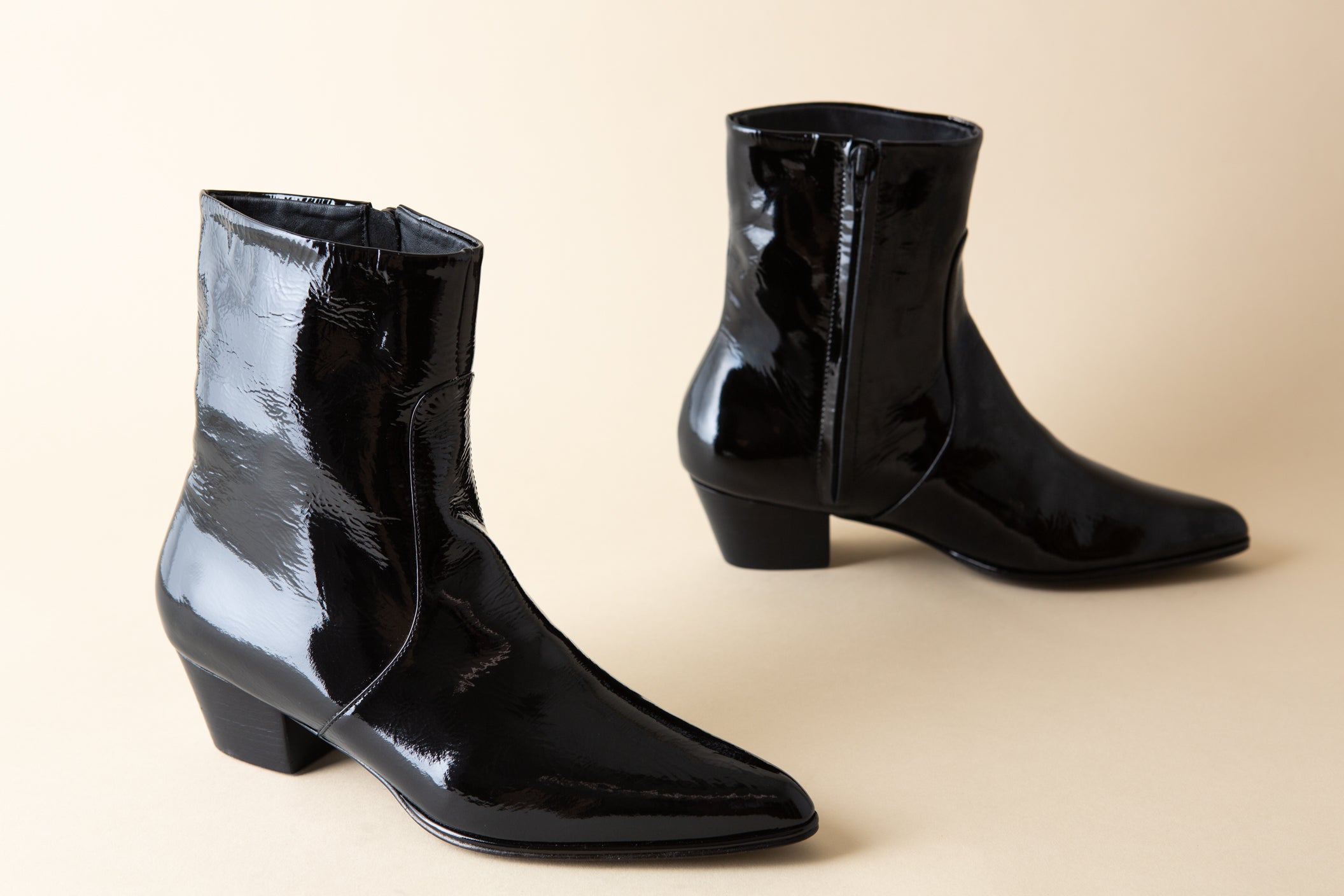 Pair of black patent leather ankle boots on a beige background