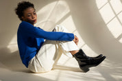 Person wearing a blue sweater and white pants sitting on a white floor with shadows cast by a window.