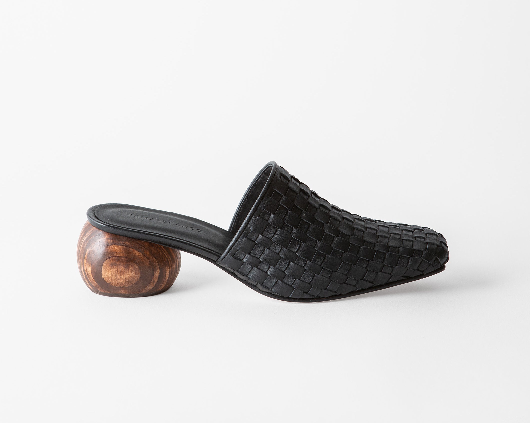 A single black woven leather mule slide with a sculptural round wooden heel, shown in profile against a clean white background.