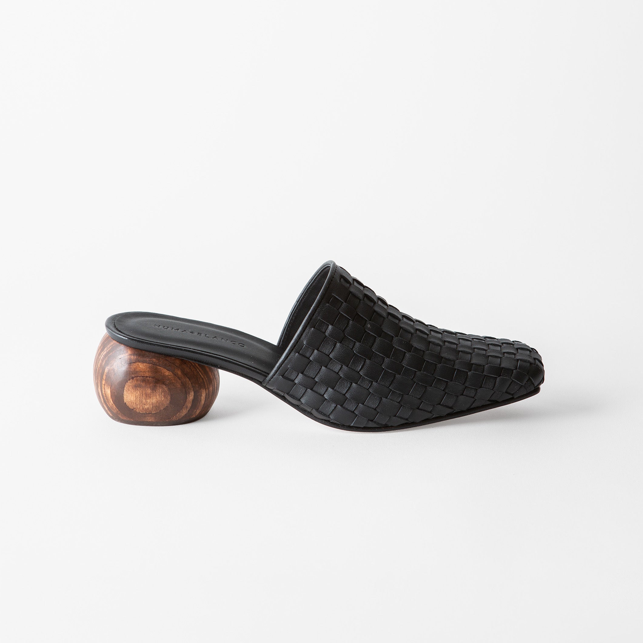 A single black woven leather mule slide with a sculptural round wooden heel, shown in profile against a clean white background.