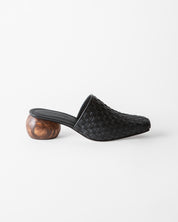 A single black woven leather mule slide with a sculptural round wooden heel, shown in profile against a clean white background.