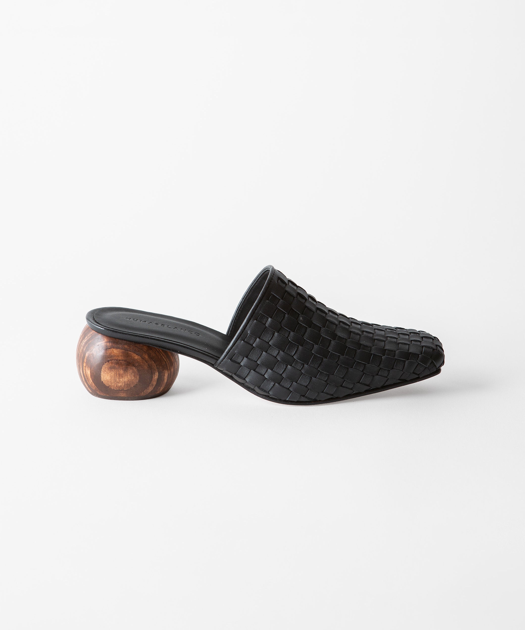 A single black woven leather mule slide with a sculptural round wooden heel, shown in profile against a clean white background.