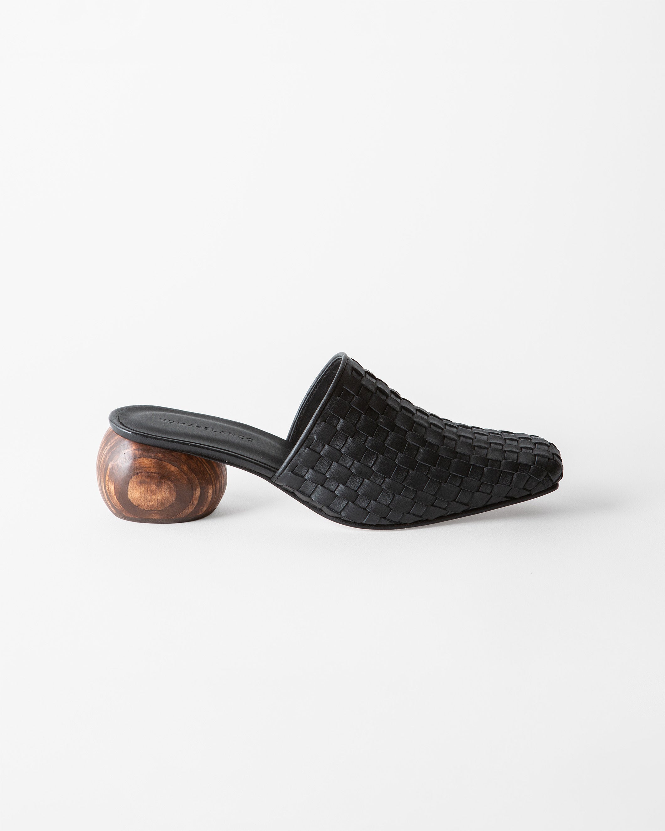 A single black woven leather mule slide with a sculptural round wooden heel, shown in profile against a clean white background.