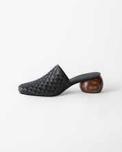 A black woven leather mule slipper with a chunky, spherical wooden block heel, shown from a side profile on a clean white background.