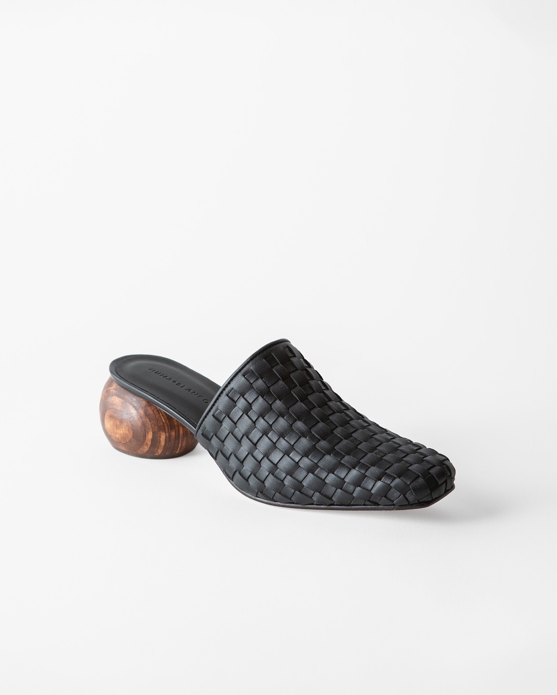 A single black woven leather mule slide with a chunky wooden block heel, shown from a side profile on a clean white background.