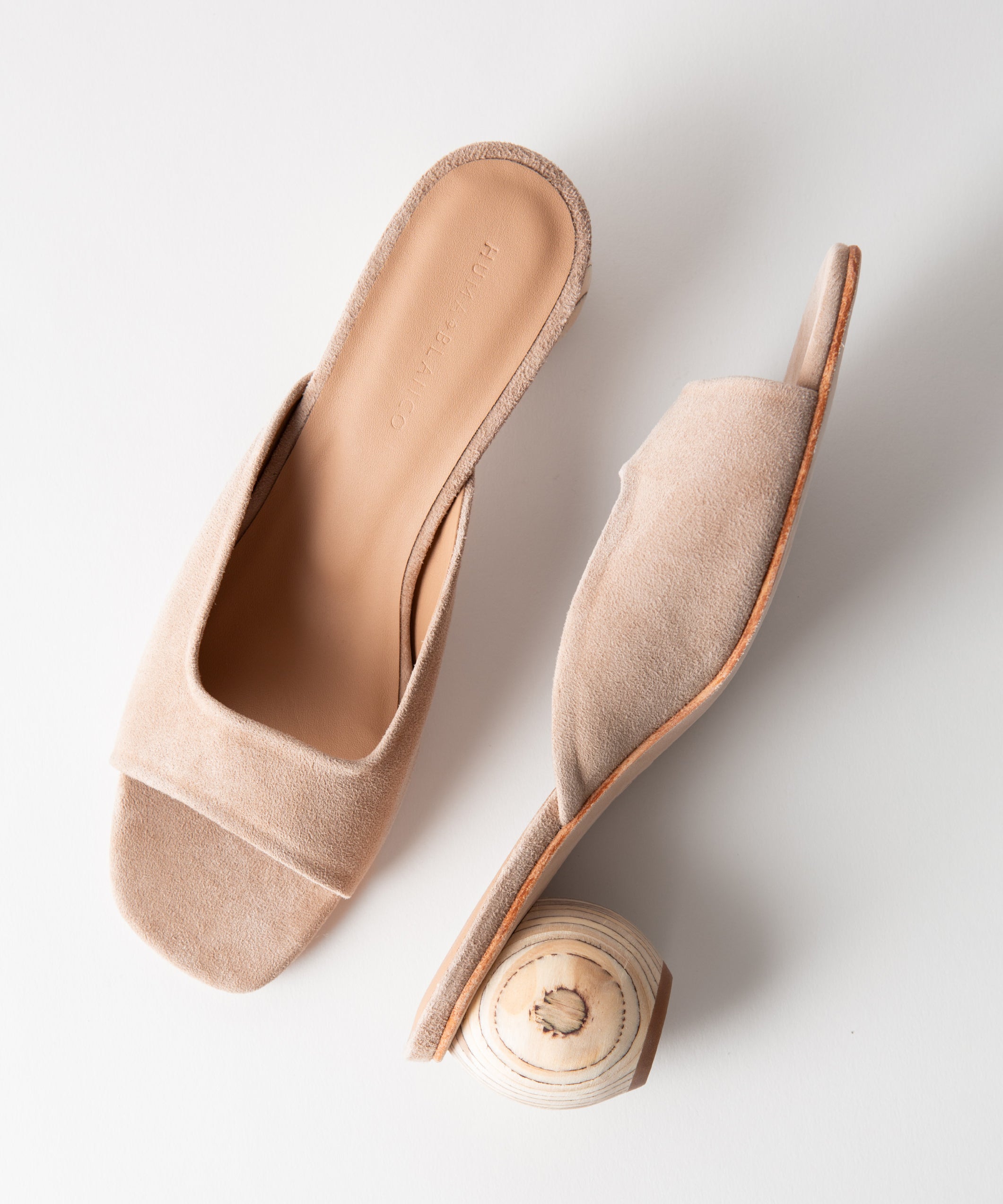Pair of beige sandals with a wood heel on a light gray background