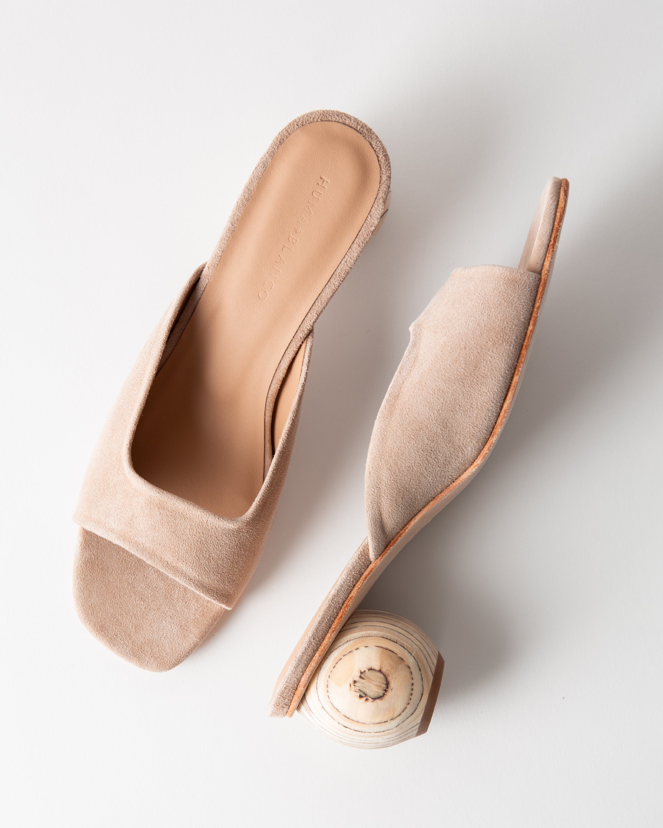 Pair of beige sandals with a wood heel on a light gray background