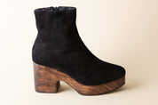 Black suede ankle boot with wooden platform sole on a beige background