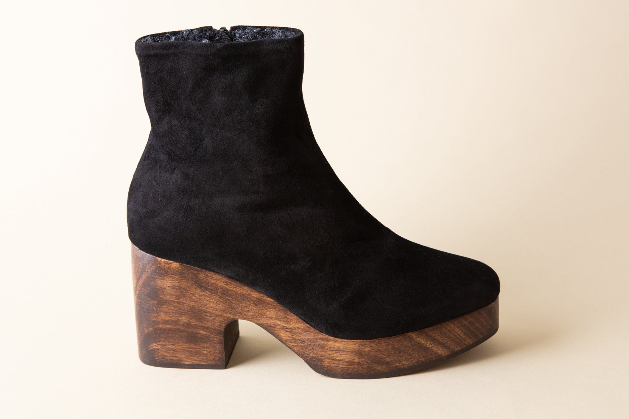 Black suede ankle boot with wooden platform sole on a beige background