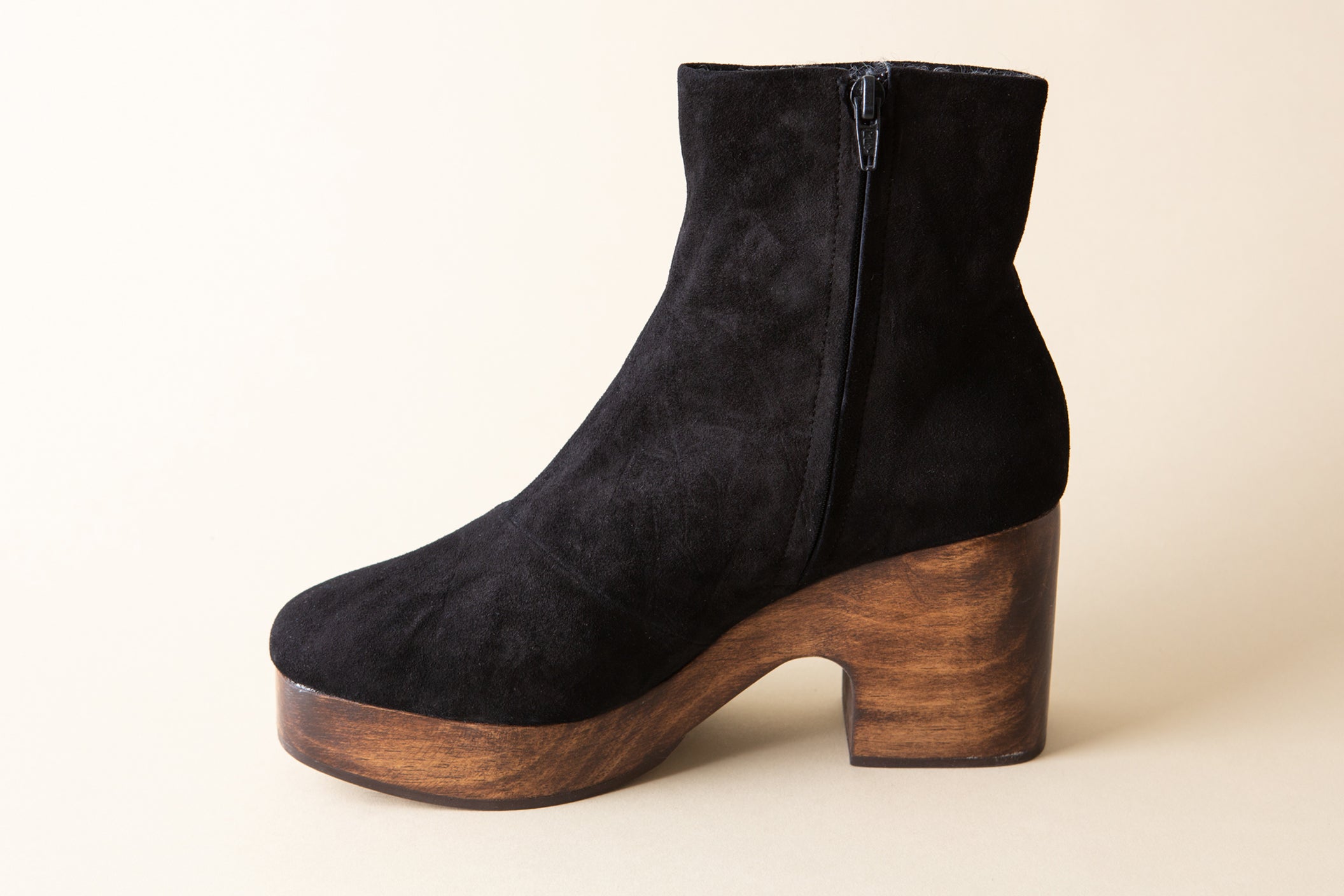 Black suede ankle boot with wooden platform sole on a beige background