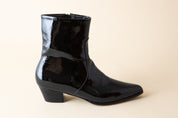 Black patent leather ankle boot on a beige background