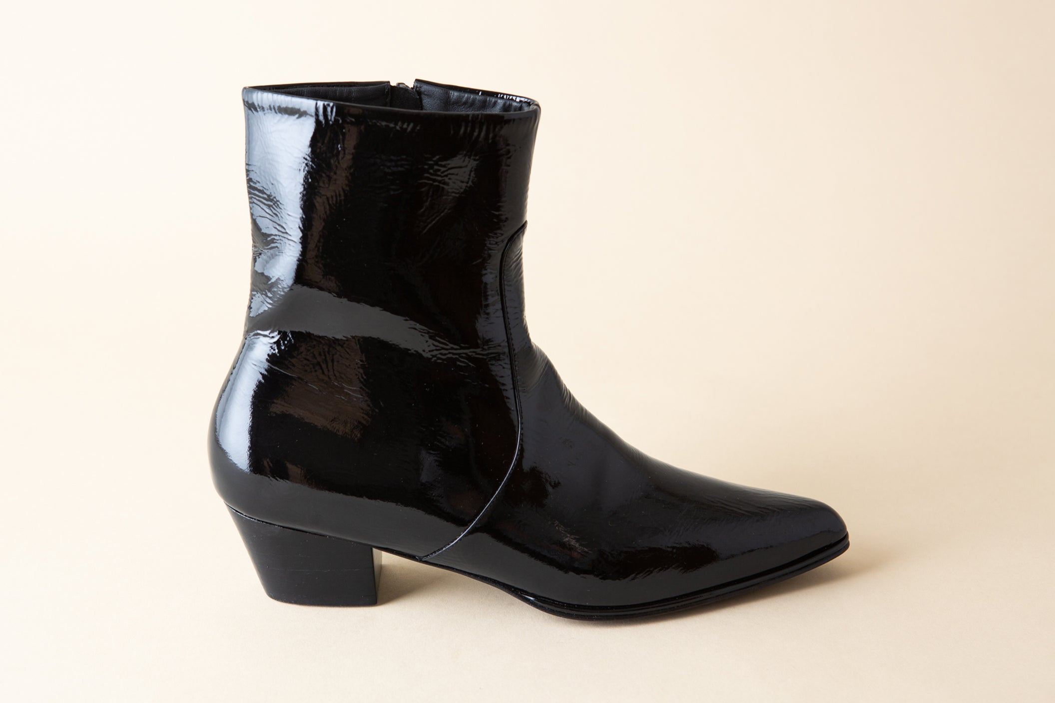 Black patent leather ankle boot on a beige background