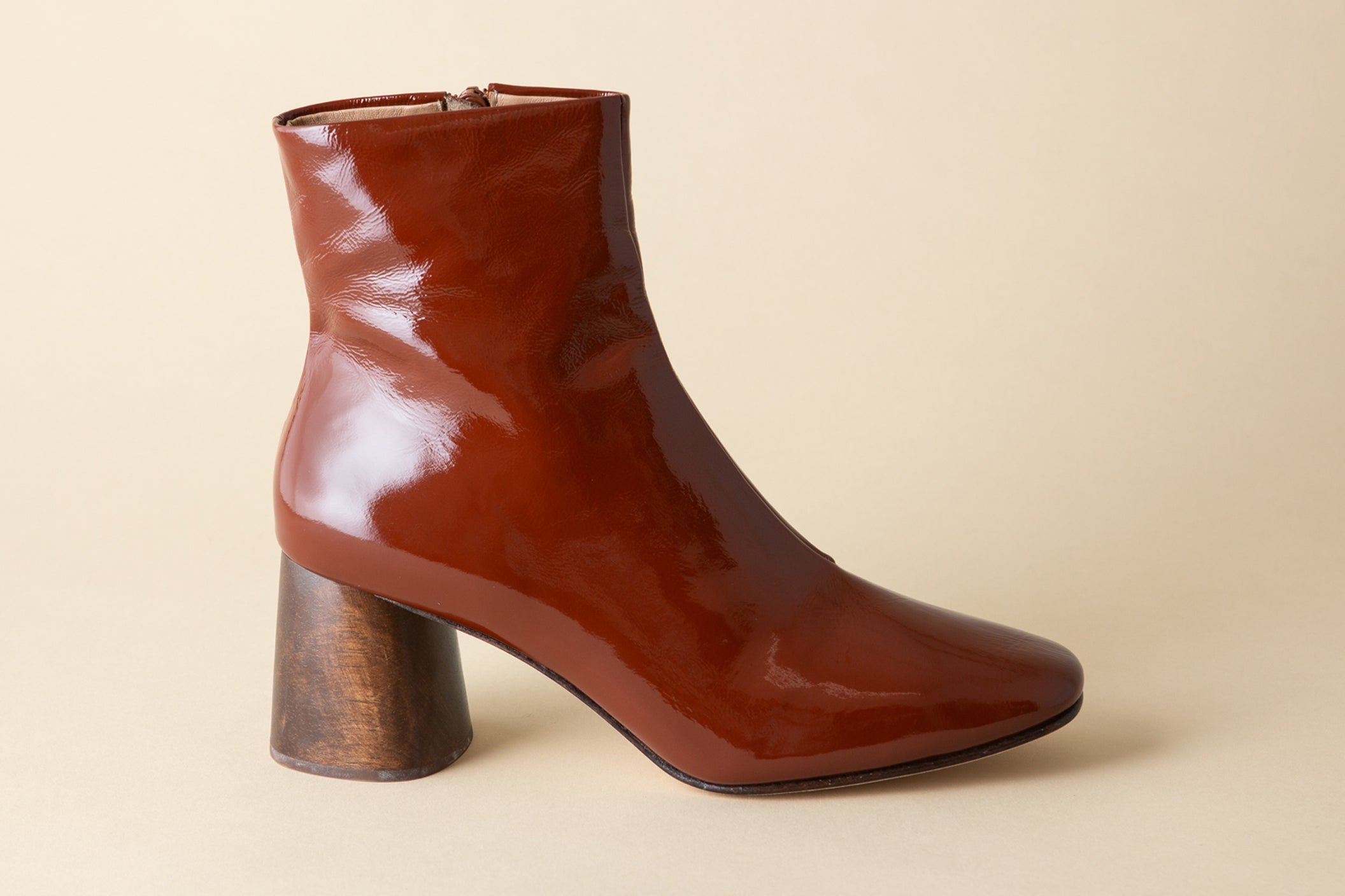 Brown patent leather ankle boot with a wooden block heel on a beige background